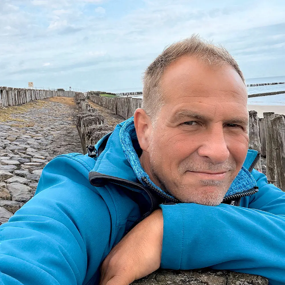 Achim Loobes lehnt entspannt am Wellenbrecher am Meer in Breskens – mit Blick in die Kamera, ruhig und fokussiert