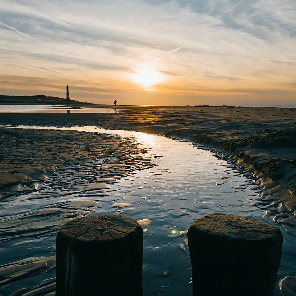 Sonnenuntergang am Strand von Breskens mit Leuchtturm und Buhnen im Gegenlicht